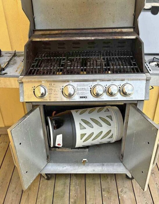 Gasoltub liggandes inuti ett underskåp i en grill med öppen dörr. Grillens vänstra gavel syns till vänster.