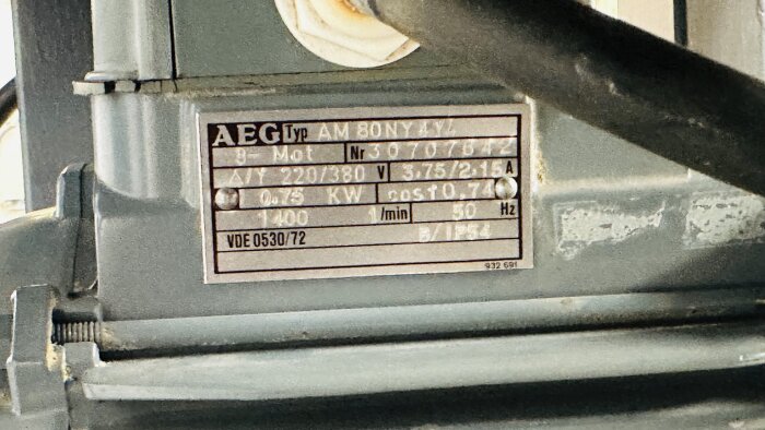 Närbild av en skylt på en motor av typen AEG AM 80NY 4Y, med specifikationer som inkluderar motorns nummer, effekt, spänning, frekvens, och varvtal.