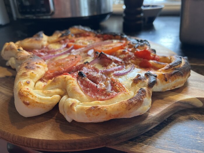 Hemlagad pizza med pålägg såsom tomatsås, mozzarella, rödlök, salami och färska tomater, delvis bränd och ojämnt gräddad, serverad på en träskärbräda.