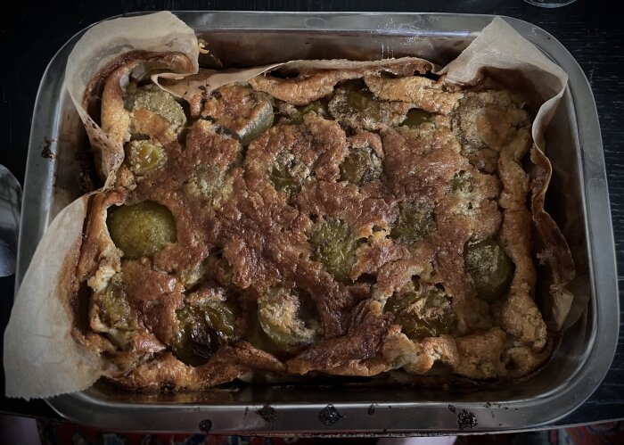 En nybakad clafoutis med plommon, rom, kanel och mandelmassa serverad i en rektangulär form med bakplåtspapper.