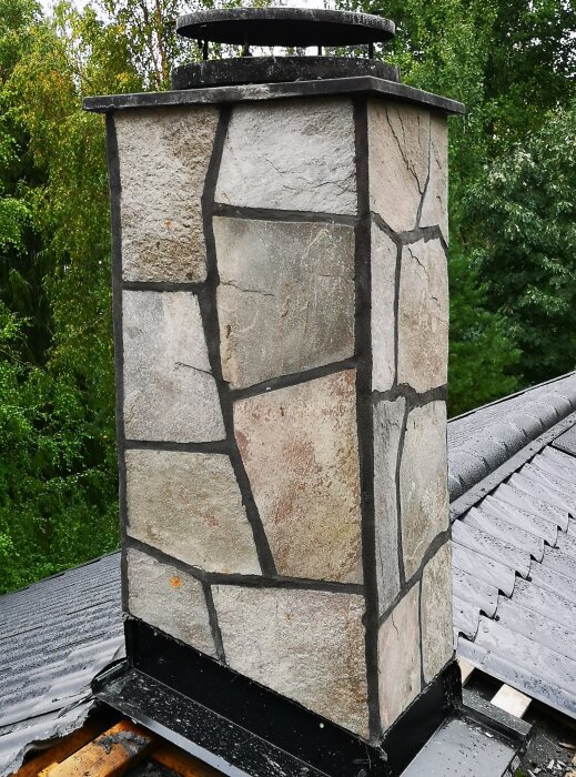 Chimney clad in used Glava slate on a roof, with green trees in the background.