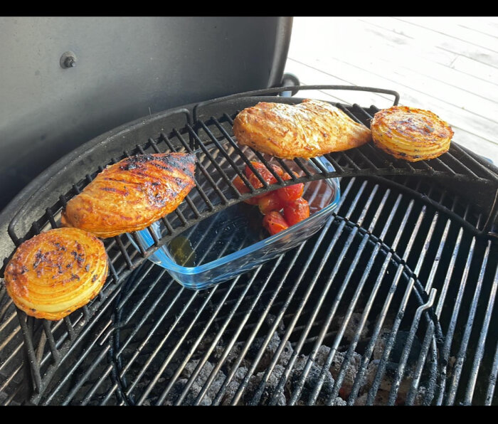 Grill med kycklingfiléer, lökar och tomater i en glasform på grillgallret.