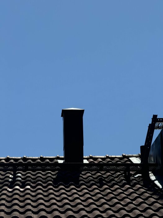 Ventilationskanal och takhuv på ett tegeltak under klarblå himmel.