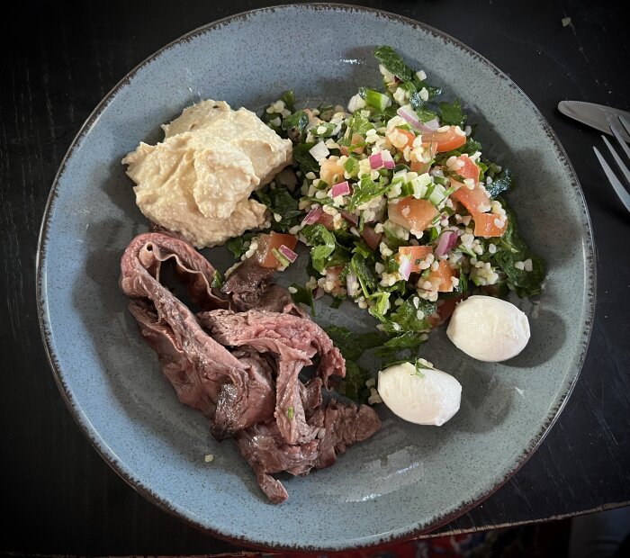 En tallrik med grillad flapstek, tabbouleh, hummus och två mozzarellabollar.