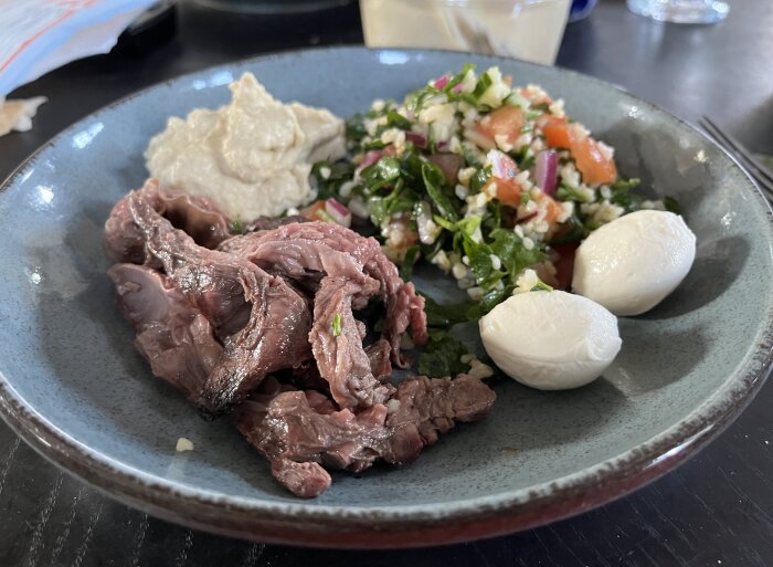 En tallrik med grillad flapstek, tabbouleh, hummus och två mozzarellabollar.