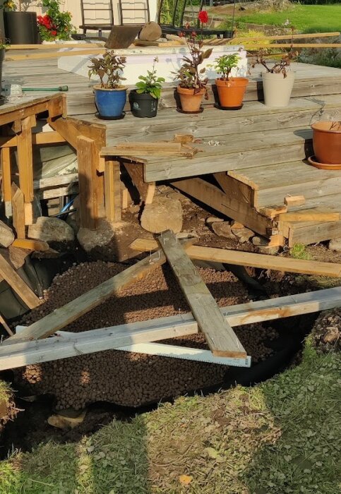 Påbörjad grundläggning med lecakulor under en altan där delar av trappen har tagits bort. Flera förberedelser är gjorda inför installationen av en badtunna.