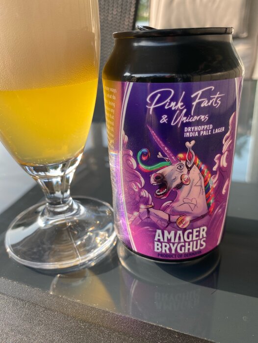 Amager Bryghus' ölburk "Pink Farts & Unicorns" samt ett glas med gyllengul öl på ett bord.