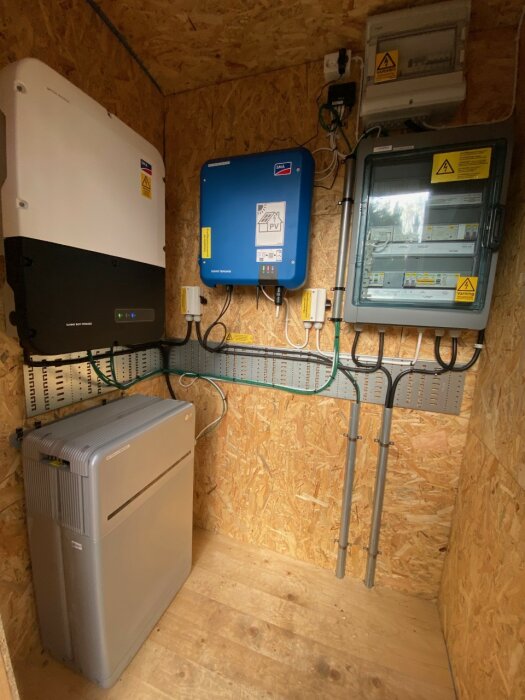 Installationen av solcells- och batteri-inverter i fritidshus, med grå Enwitec-skåp för nödström, blå SMA Tripower och svart/vita SMA Sunny Boy Storage.