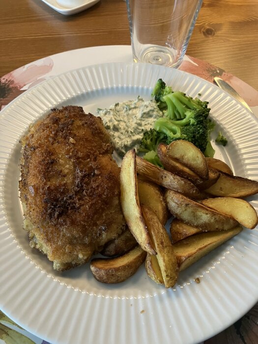 Kyckling Kiev serverad med klyftpotatis, broccolibitar och örtmajonnäs på en vit tallrik.