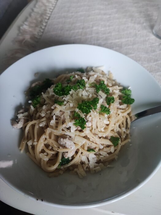 En skål med spagetti blandad med citronkyckling, toppad med riven parmesanost och persilja.