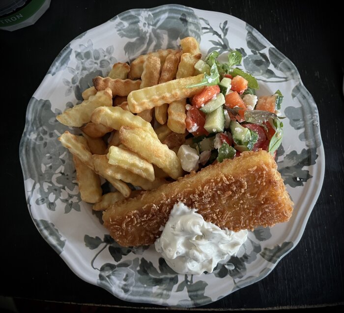 En tallrik med panerad fisk, krispiga pommes frites, sallad med grönsaker och citron- och dillsås.