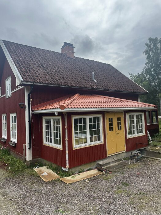 Ett rött hus med en nybyggd utbyggnad med valmat tak och gula dubbeldörrar, fotograferat mot en molnig himmel. Träfiberisolering diskuteras i inlägget.