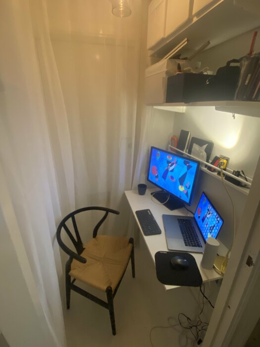 Litet kontor inrett i en oanvänd entré, med ett skrivbord, en stol, en dator, en laptop och hyllor ovanför. Dator- och laptorskärmarna visar båda samma bakgrundsbild.