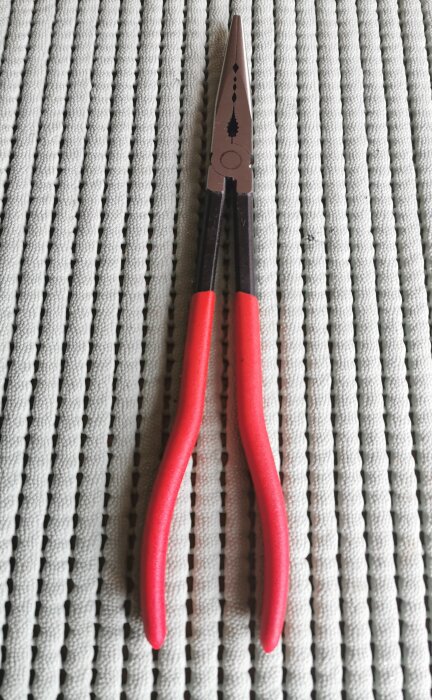 Knipex-tång med röda handtag ligger på en vit ribbad matta.