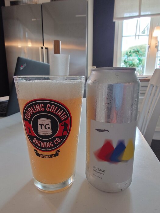 Ett glas med öl från Toppling Goliath Brewing Co. bredvid en burk av Selfsame India Pale Ale från Finback, på ett bord i ett modernt kök.