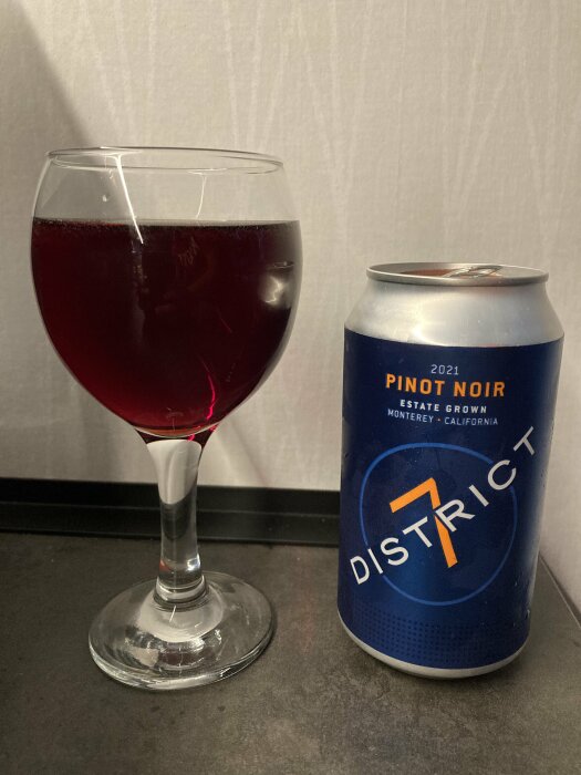 Ett glas med rött vin bredvid en burk District 7 Pinot Noir vin från 2021.