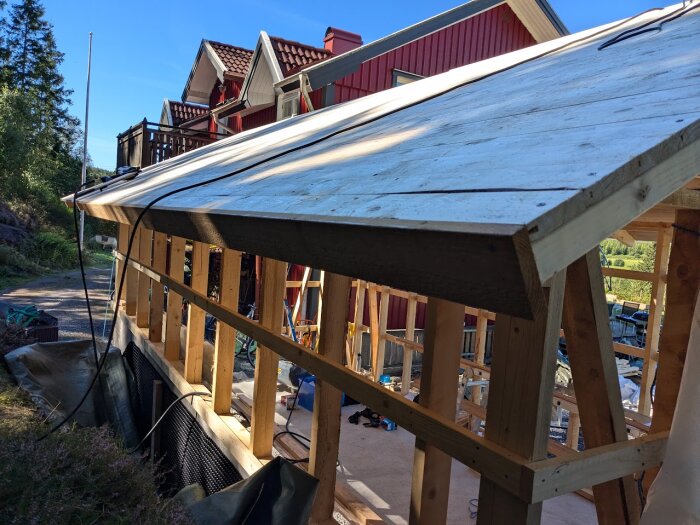 Råsponttak under uppbyggnad med fastskruvad takfotsbräda. Vitt hus och skog i bakgrunden.