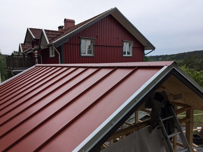 Nytt rött klicktak på en byggnad under renovering, med en äldre röd villa i bakgrunden.