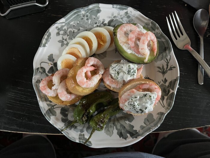 En tallrik med räkor på avokado och bröd med örtröra, kokta ägg och stekta pimientos de Padrón.