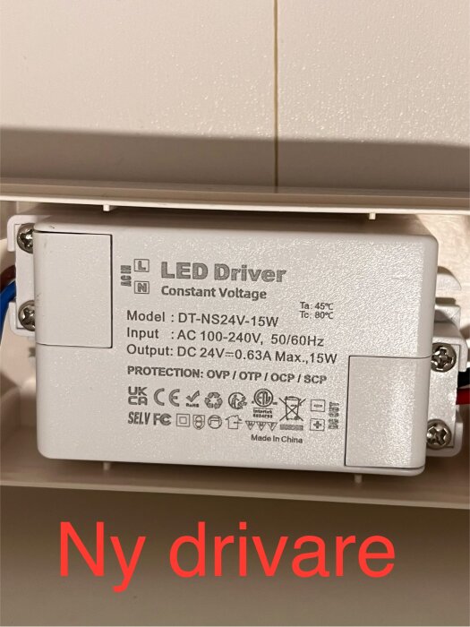 Ny LED-drivare av modellen DT-NS24V-15W som visar input och output specifikationer, monterad i ett badrumsskåp med texten "Ny drivare" i rött.