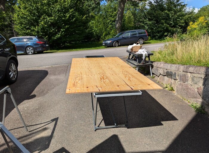 Plywoodskiva på ett tillfälligt arbetsbord, utomhus vid en asfalterad väg med bilar i bakgrunden, för ett platsbyggt förvaringsprojekt.