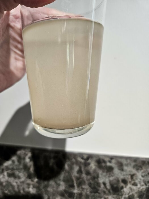 Muddy and discolored water in a clear glass, illustrating water quality issues from a newly drilled well.