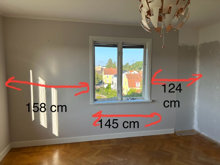 Tomt sovrum med nymålande väggar och golv i fiskbensparkett, måttangivelser (158 cm, 124 cm och 445 cm) i rött på väggarna och kring ett fönster.