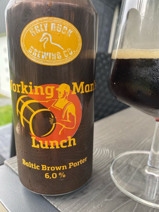 En burk porteröl från Ugly Duck Brewing Co. med texten "Working Man's Lunch, Baltic Brown Porter 6,0%" bredvid ett glas med mörkt öl.