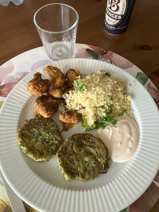 En tallrik med friterade blomkålsbuketter, zucchinibiffar, couscous med paprika och lök samt yoghurtsås med sriracha och citron.