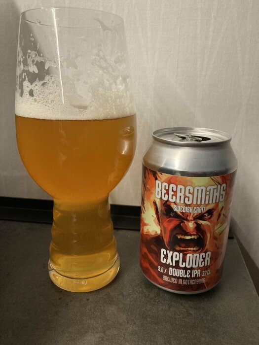 En glas öl med skumkrona bredvid en burk Beersmiths Exploder Double IPA, Swedish Craft, med en agiterad man på etiketten.