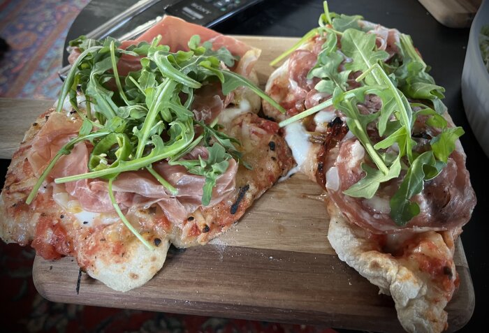 Hemgjorda pizzor med mozzarella, serranoskinka, ruccola och tomatsås på en träskärbräda.