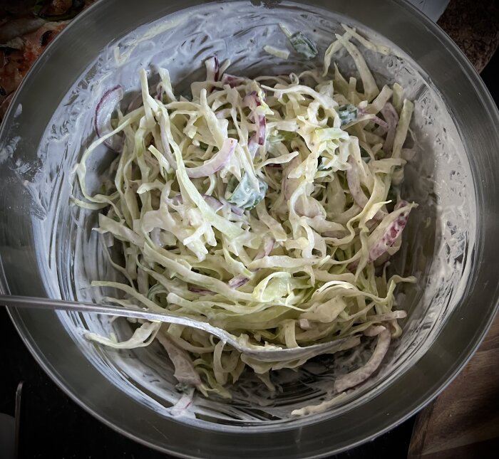 Coleslaw med salladslök och rödlök i en rostfri skål redo att serveras tillsammans med hemlagad pizza.