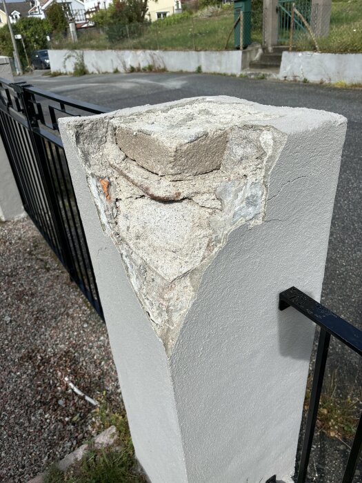 Sprucken murad grindstolpe med skador och löst material som behöver åtgärdas. Grinden och omgivande trottoar syns i bakgrunden.