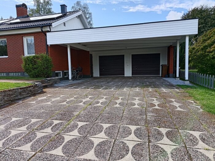 Bild av ett tegelhus med carport och nybyggd uppfart, prydd med mönstrade betongplattor. Två cyklar syns parkerade i carporten.