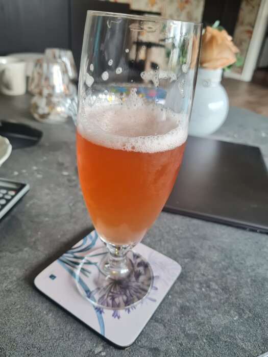 Ett glas hemmagjord Berliner Weisse med hallonsmak på ett underlägg, stående på ett bord.