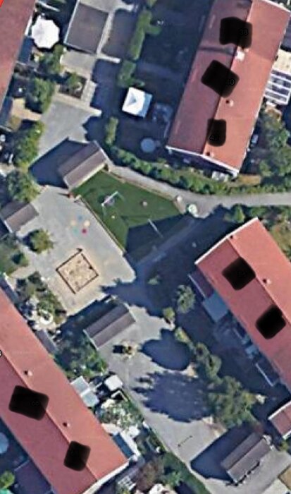 Flygfoto över innergårdar omgivna av flerbostadshus med röda tak. Gården har en lekplats, grönområde och flera gångvägar. Ingen biltrafik synlig.