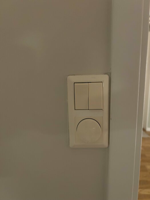 Kombinationsram med två lampknappar och en dimmer installerad på en vägg.