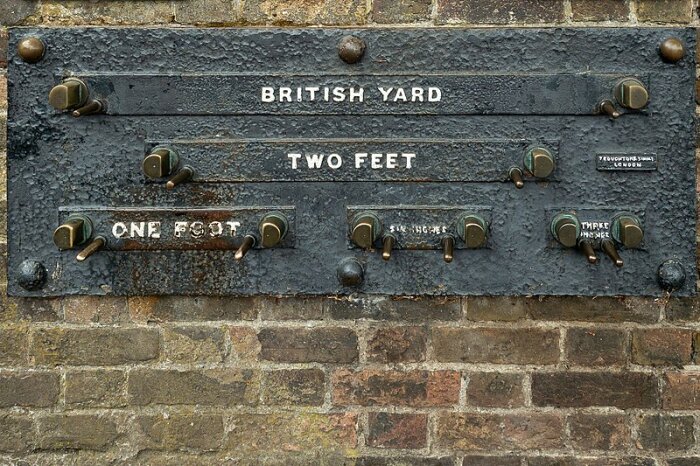 Skylt på en mur i Greenwich med referensmått: British Yard, Two Feet, One Foot, Six Inches och Three Inches, för att kontrollmäta verktyg.