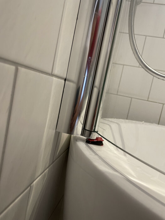 Begagnad kurvad duschvägg i metall monterad på väggen, med stöddelar av plast som är förstärkta med gummitejp och plast under den främre delen av badkarskanten.
