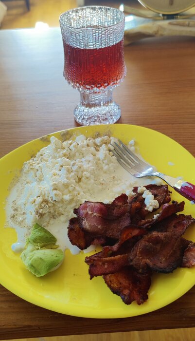 Tallrik med avocado, keso och bacon på ett träbord tillsammans med ett glas hemlagad vinbärsaft.