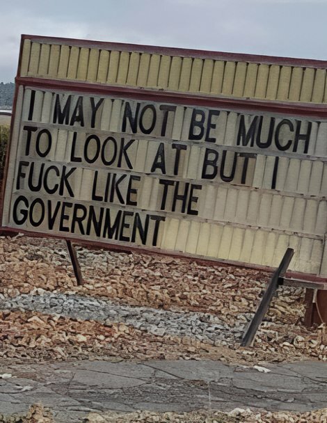 En skylt med texten "I may not be much to look at but I fuck like the government" står lutad på marken.