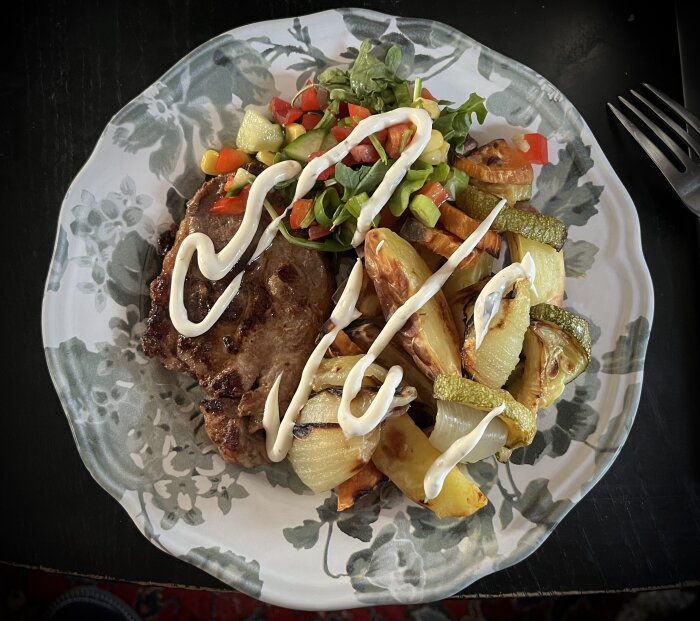 Tallrik med fläskkarré, ugnsstekta grönsaker och potatis, sallad med paprika och salladslök, toppad med sås.