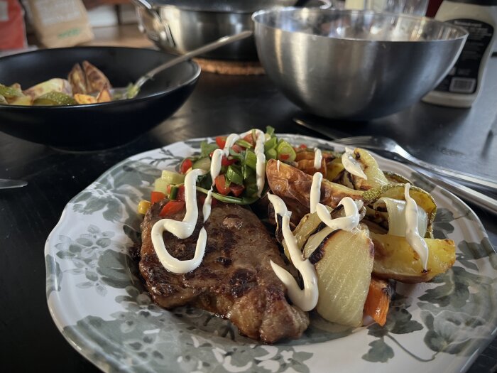 Tallrik med fläskkarré, ugnstekta grönsaker och potatis, toppad med sås, samt sallad. I bakgrunden syns skålar med ytterligare ingredienser.