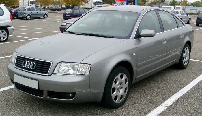 Silverfärgad Audi A6 (1997-2004) parkeras på en parkeringsplats omgiven av andra bilar, sedd från sidan framifrån.