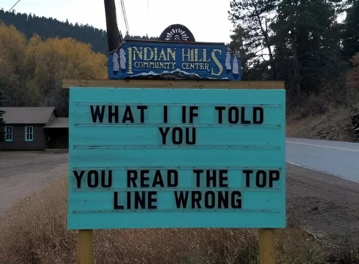 Skylt utanför Indian Hills Community Center med texten "WHAT I IF TOLD YOU YOU READ THE TOP LINE WRONG" som skapar en optisk illusion.