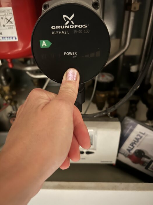 En hand pekar på en Grundfos ALPHA2 L cirkulationspump med texten "POWER ON".