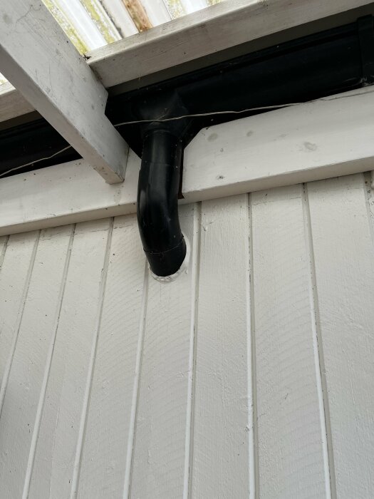 Svart stuprör som går genom en vit vägg i en carport med överliggande plasttak.