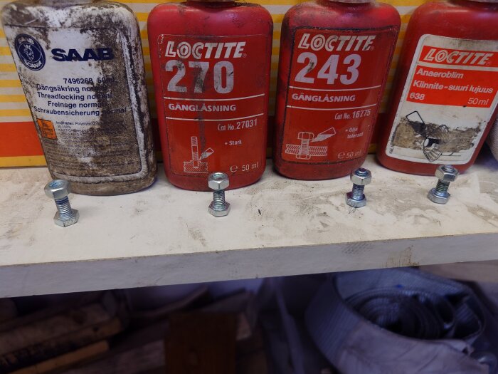 Fyra flaskor gängsäkring, märkena SAAB, Loctite 270, Loctite 243 och Loctite 638, placerade på en hylla med fyra bultar framför sig.