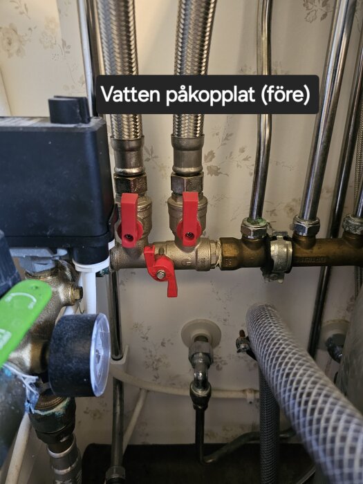 Vattenanslutningar i en sommarstuga med tre röda ventiler, en tryckmätare och text "Vatten påkopplat (före)".