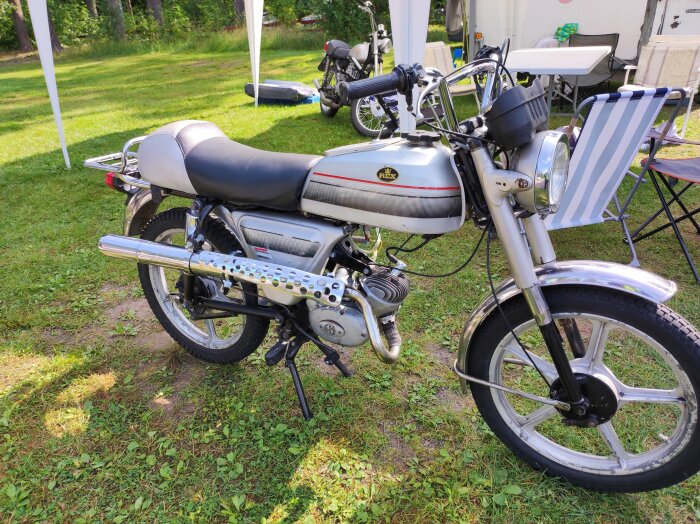 REX Sprint moped till salu, silver och svart, avbildad utomhus på gräs med en campingscen i bakgrunden.